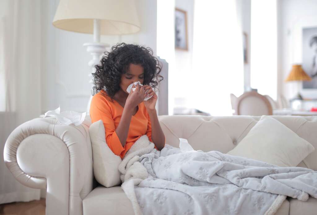 Women on couch with blanket blowing her nose