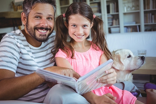 Man and daughter read a book while dog looks on