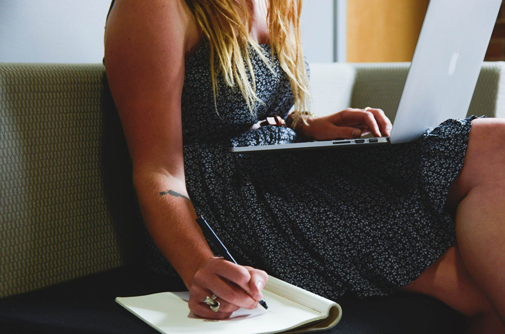Young woman does research on a laptop and takes notes