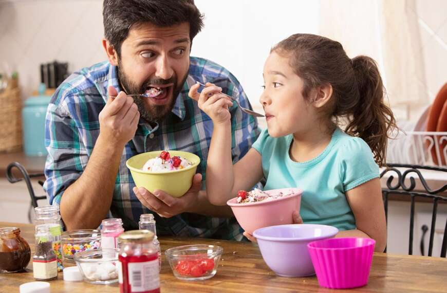 Dad and daughter laugh together over ice cream sundaes, enjoying Summer vacation comfortably at home - the way it should be. Find out how All American Heating can help you make sure your home cooling system is the most energy-efficient it can be.
